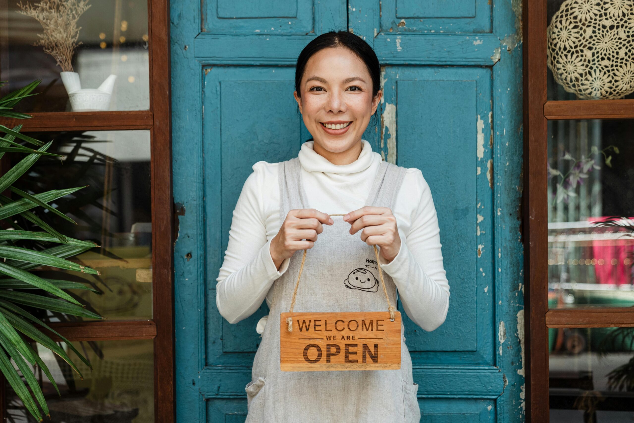 Women standing in front of her sole proprietorship holding a welcome sign